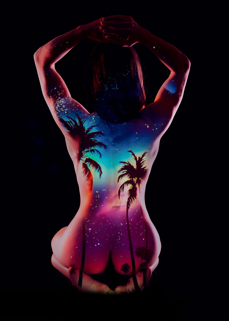 Nude person kneeling with arms raised behind head and a colorful cosmic sunset, stars, and palm tree scene projected onto their back and legs against a black background.