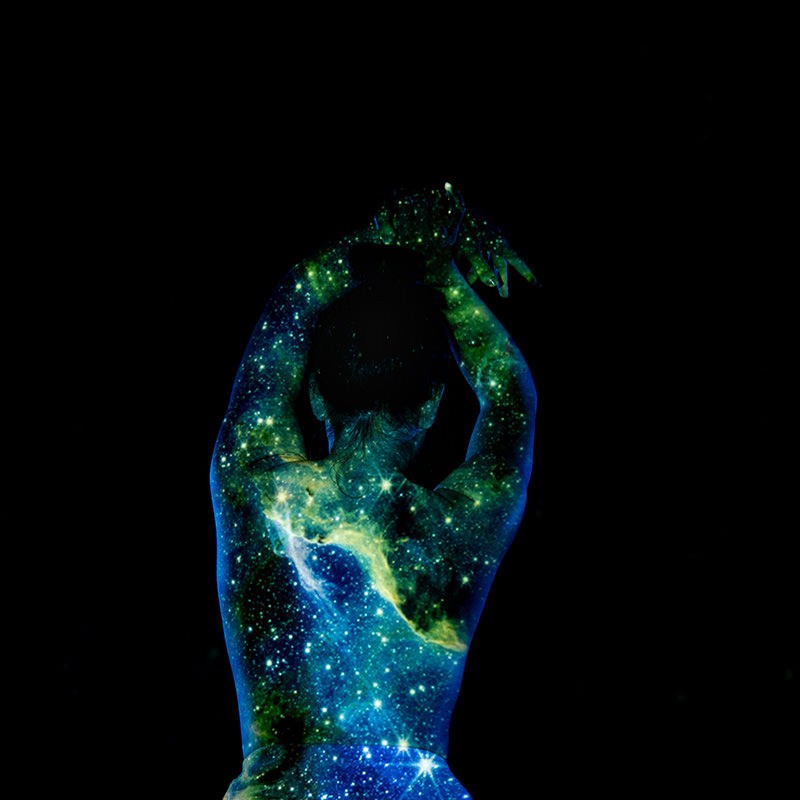 Back view of a person standing with arms raised and hands clasped overhead, their body illuminated and overlaid with a vibrant star-filled galaxy pattern against a solid black background