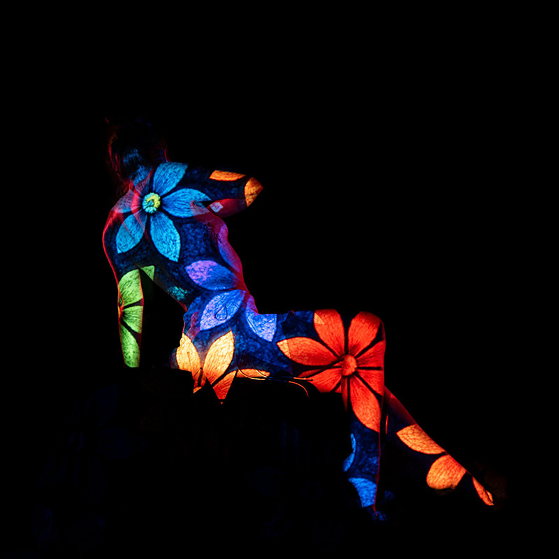 Seated person with body covered in colorful flower projections against black background