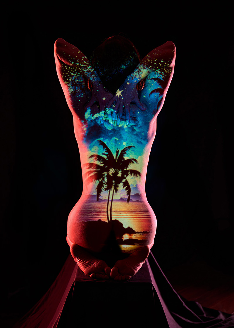 Nude person sitting on knees with arms bent behind head, tropical sunset with palm trees and starry sky projected onto their back