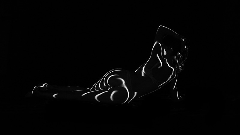 Person lying on their side with abstract curved white light patterns projected on their body against a black background