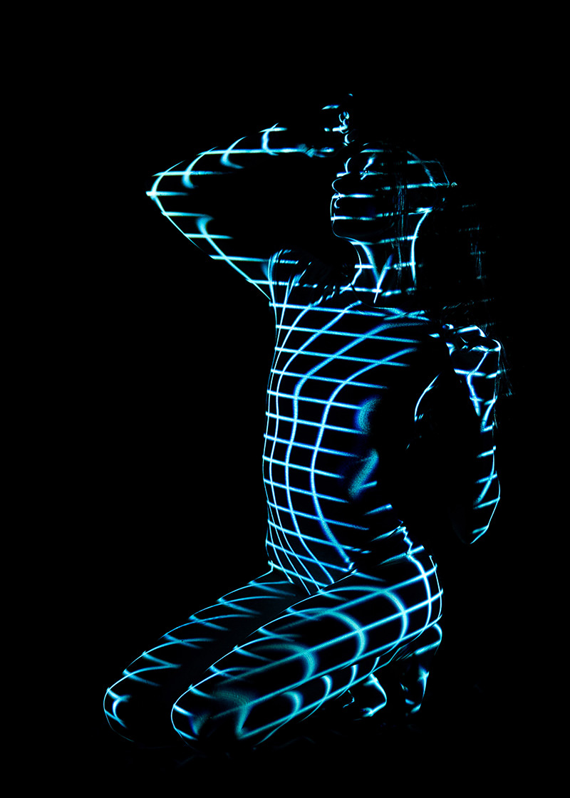 Person kneeling with a grid pattern of blue light projected across their body against a black background