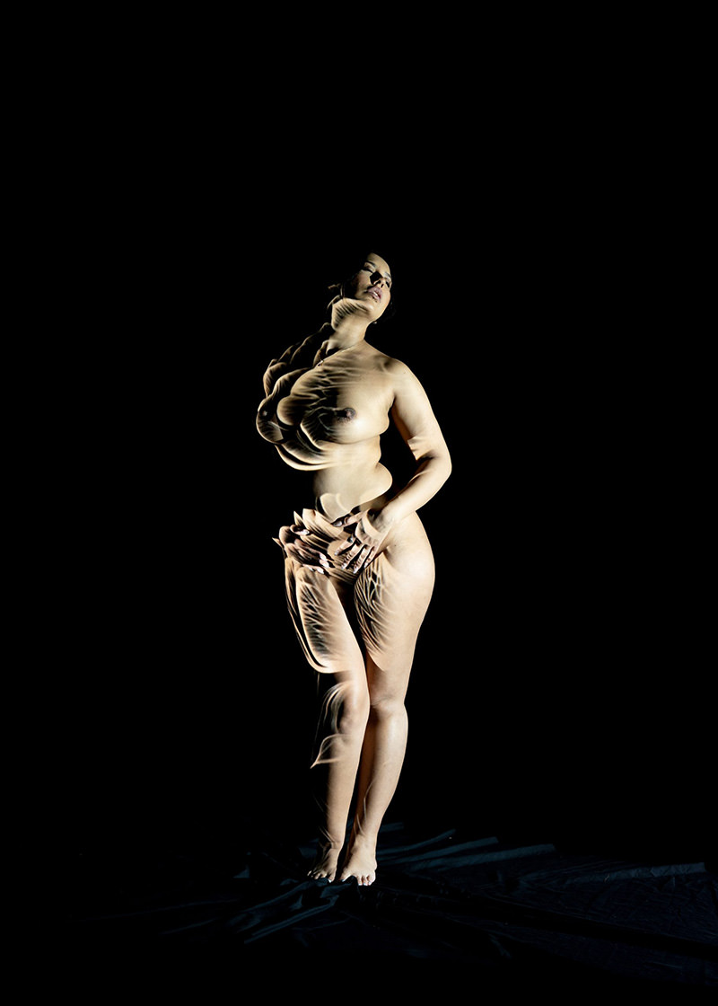Nude person standing against a dark background with multiple distorted light patterns creating an abstract visual effect over their body