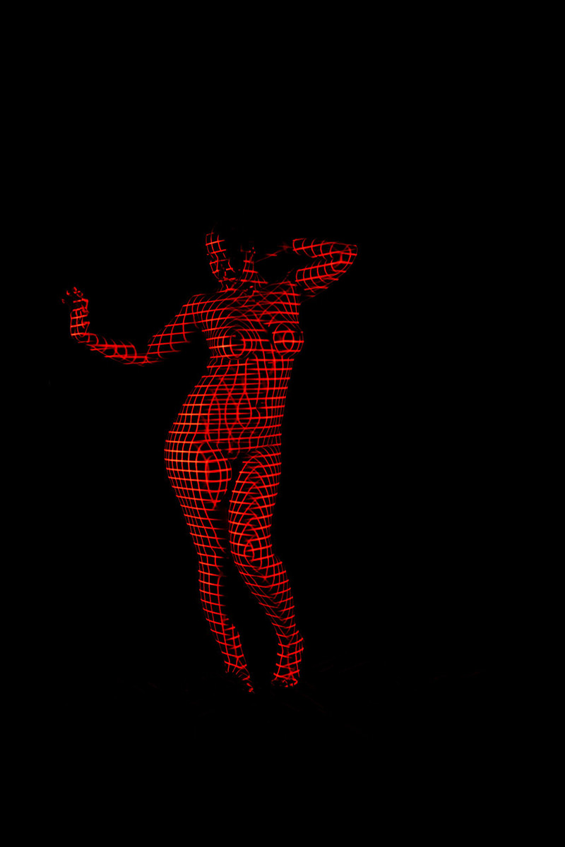 Nude person posed against black background with red grid pattern projected over their entire body, creating a three-dimensional effect