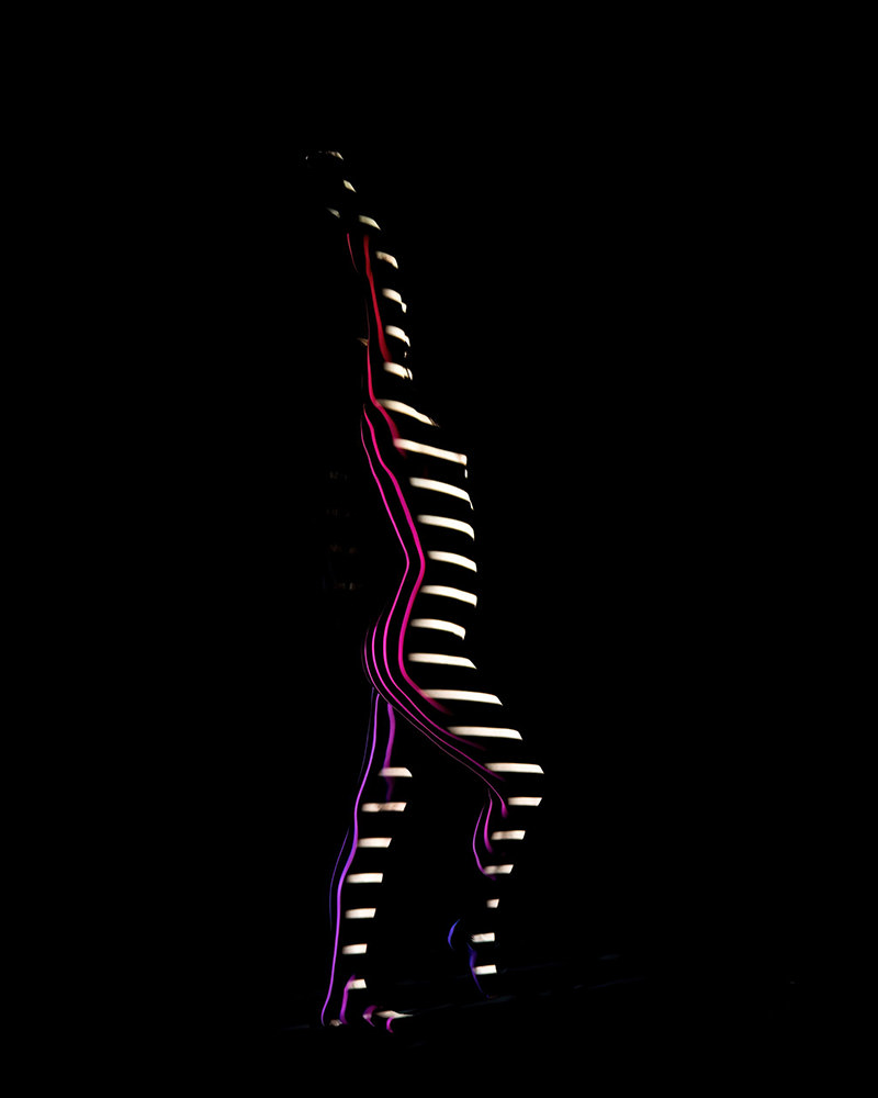 Human figure outlined by alternating horizontal white and thin colored stripes of light on a black background, emphasizing the contours of the body and creating an abstract visual effect