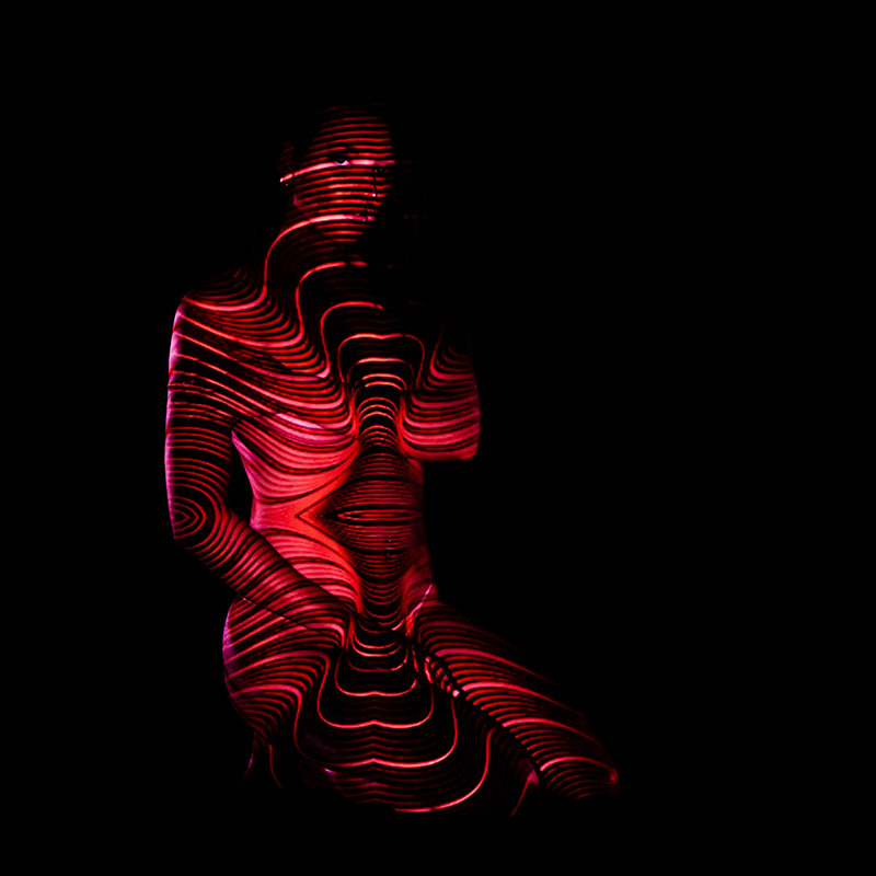 Nude person with red, wavy horizontal light patterns projected on their body, against a black background