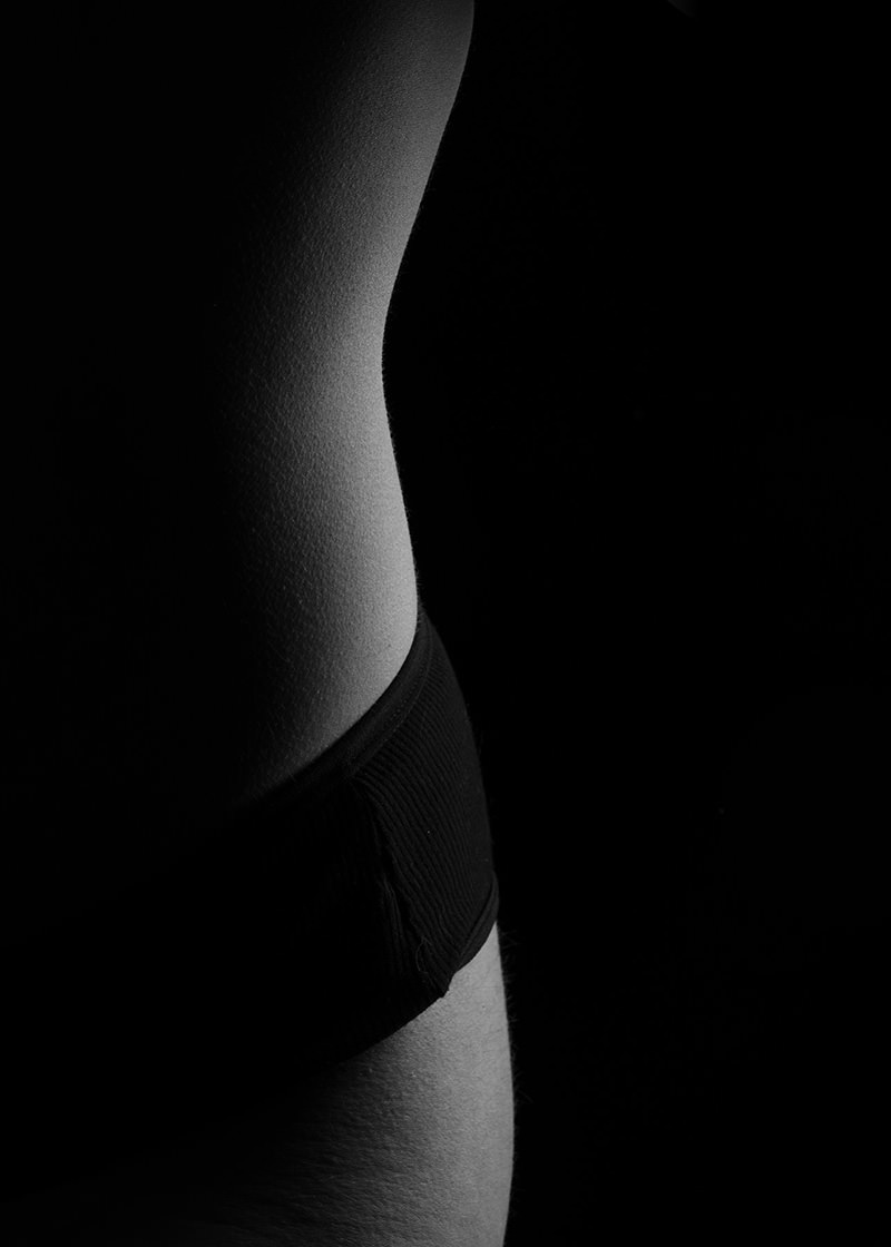 Side view of a person's torso illuminated by soft light, wearing dark underwear against a black background