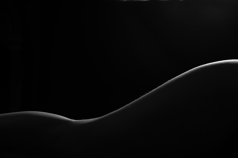 Curved human form highlighted by gentle light against a dark background