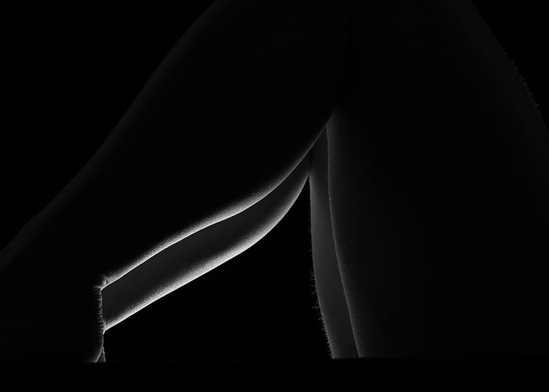 Close-up of bent legs with delicate backlighting emphasizing smooth skin texture and outlines against a black background
