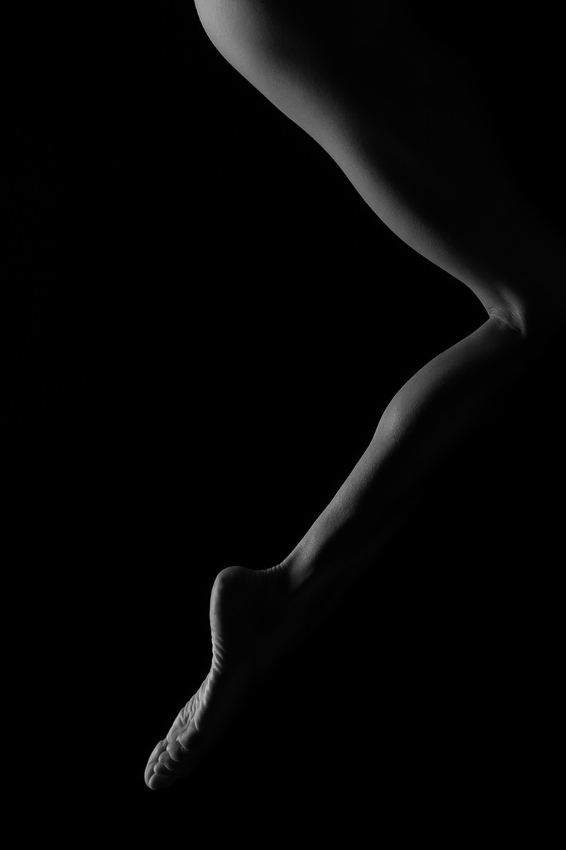 Close-up of a bent human leg and foot illuminated gently against a black background