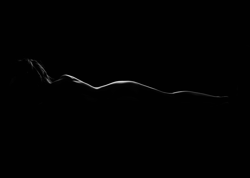 A reclining human figure shown in silhouette with light highlighting the contours of the body against a dark background