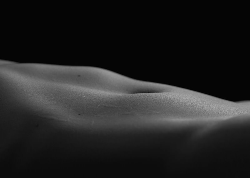 Close-up view of a human back with smooth skin and subtle shadows highlighting the natural curves against a black background