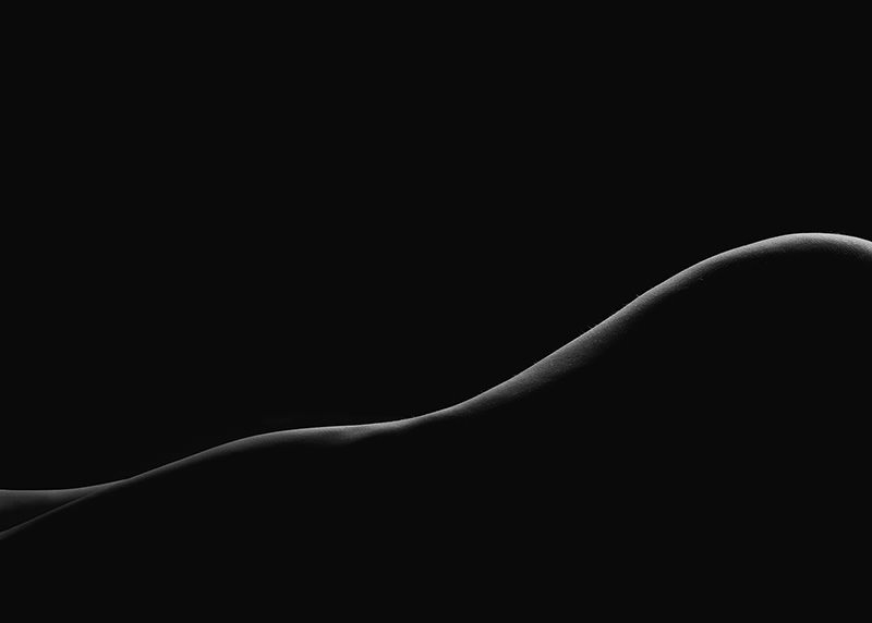 Curved silhouette of a reclining human body against a black background, highlighted by soft edge lighting