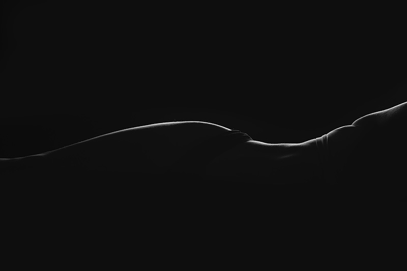 Side profile silhouette of a person lying down, highlighting the curves of their torso and hips against a black background