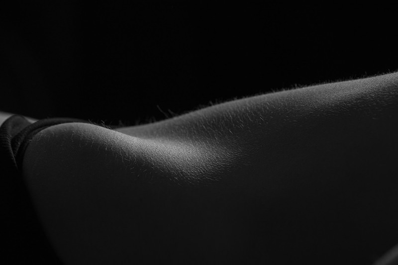Close-up of human skin illuminated by soft light, showing fine body hair and surface texture against a dark background
