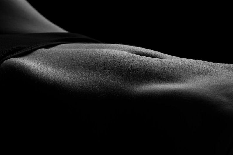 Close-up of a toned human back in low light, highlighting smooth skin texture and muscle contours against a black background