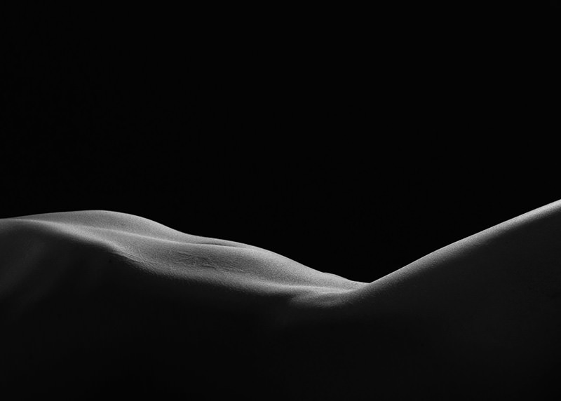 Close-up of a human torso lying down, illuminated softly to highlight smooth contours against a black background