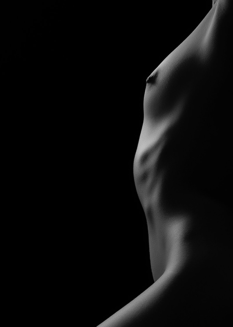 Close-up view of a male torso from the side, showcasing muscular definition and contours in black and white against a dark background