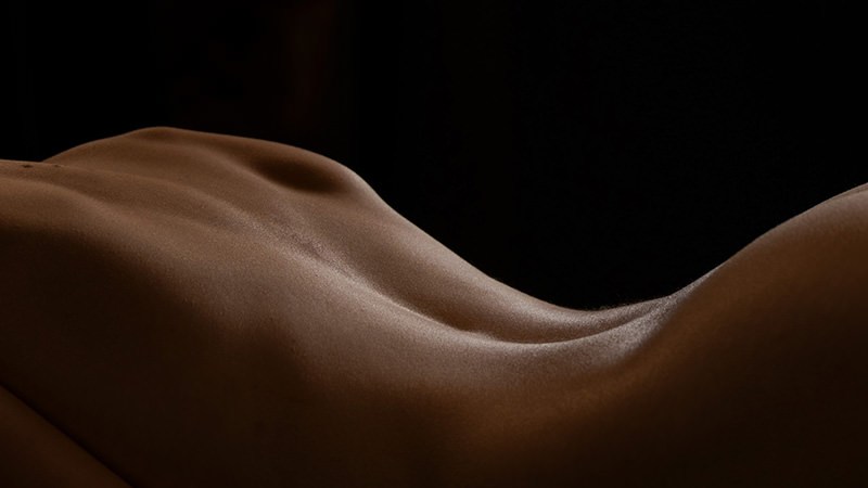 Close-up view of a smooth, toned human back with subtle muscles and spine visible, illuminated softly against a dark background