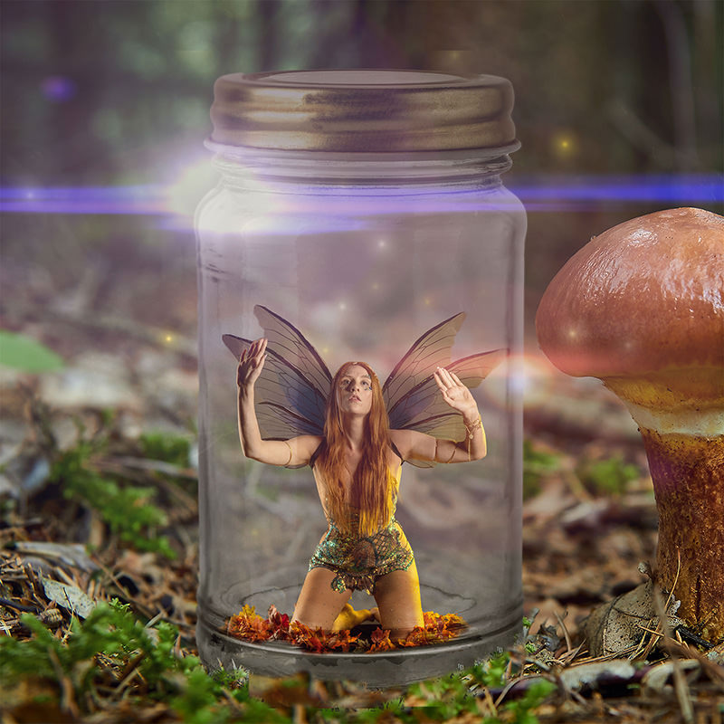 A small fairy with long red hair and delicate wings kneels inside a glass jar surrounded by autumn leaves, placed on a forest floor with a large mushroom nearby.