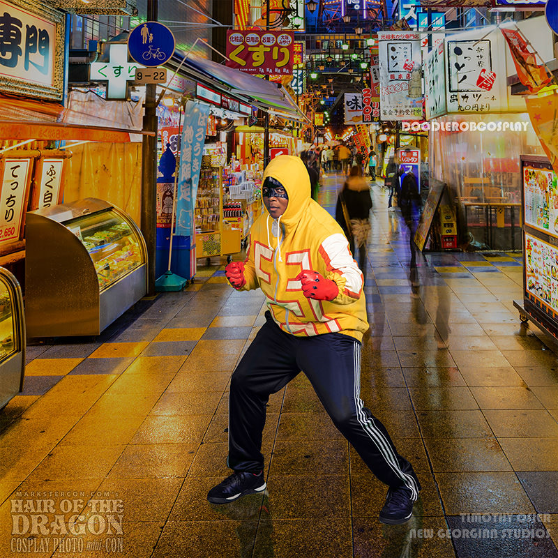 Person wearing a yellow hoodie with '53' in red, black face mask, red gloves, and black athletic pants posing with fists raised in a brightly lit street market filled with colorful neon signs and blurred pedestrians in the background