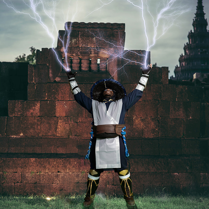 Person dressed in warrior costume with a wide-brimmed hat, raising both hands to the sky, lightning bolts emanating from their hands, standing in front of an ancient stone structure under a cloudy sky