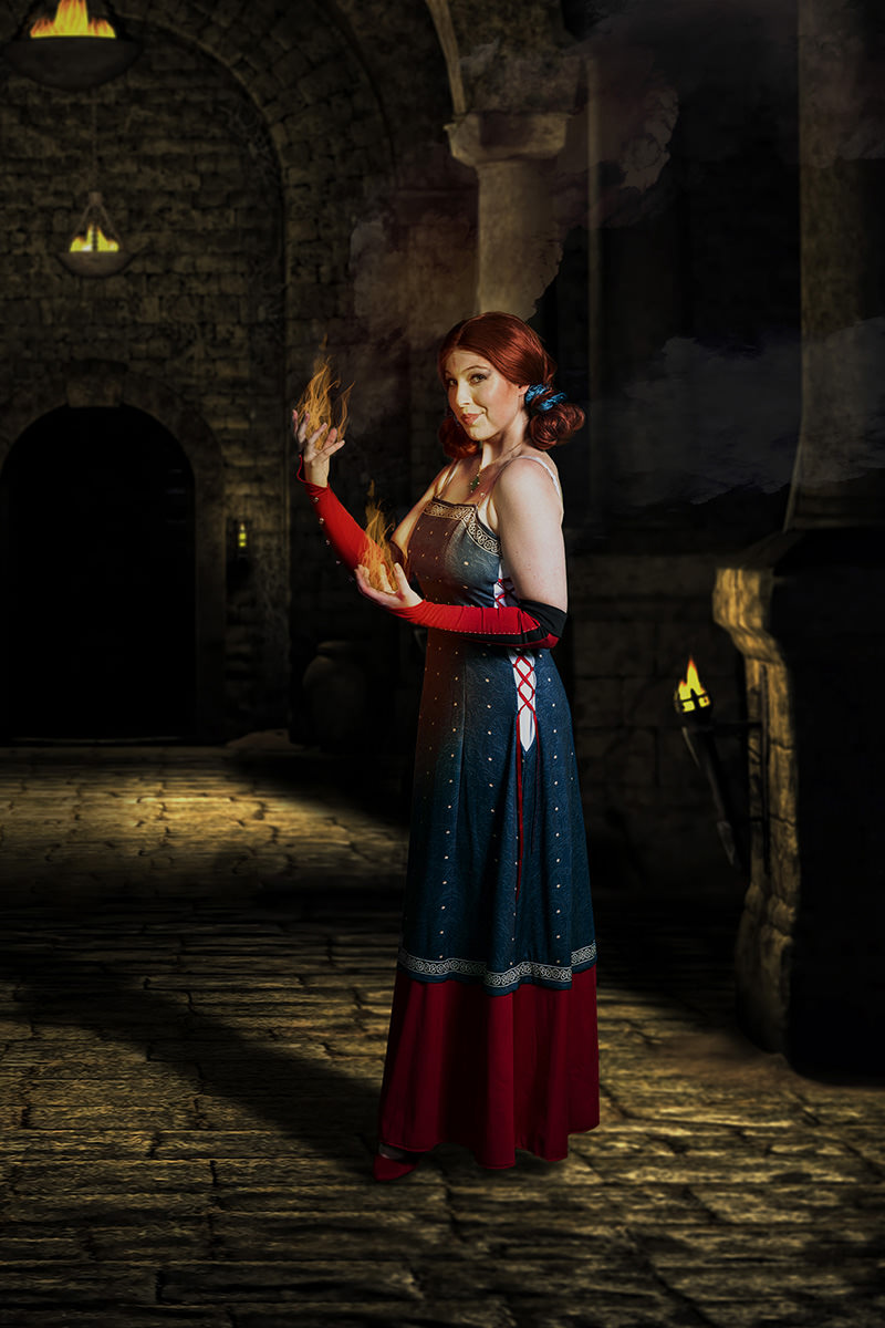 Woman with red hair styled in buns wearing a medieval-style dress with red gloves, standing in a stone-walled chamber with torches, holding magical flames in her hands.