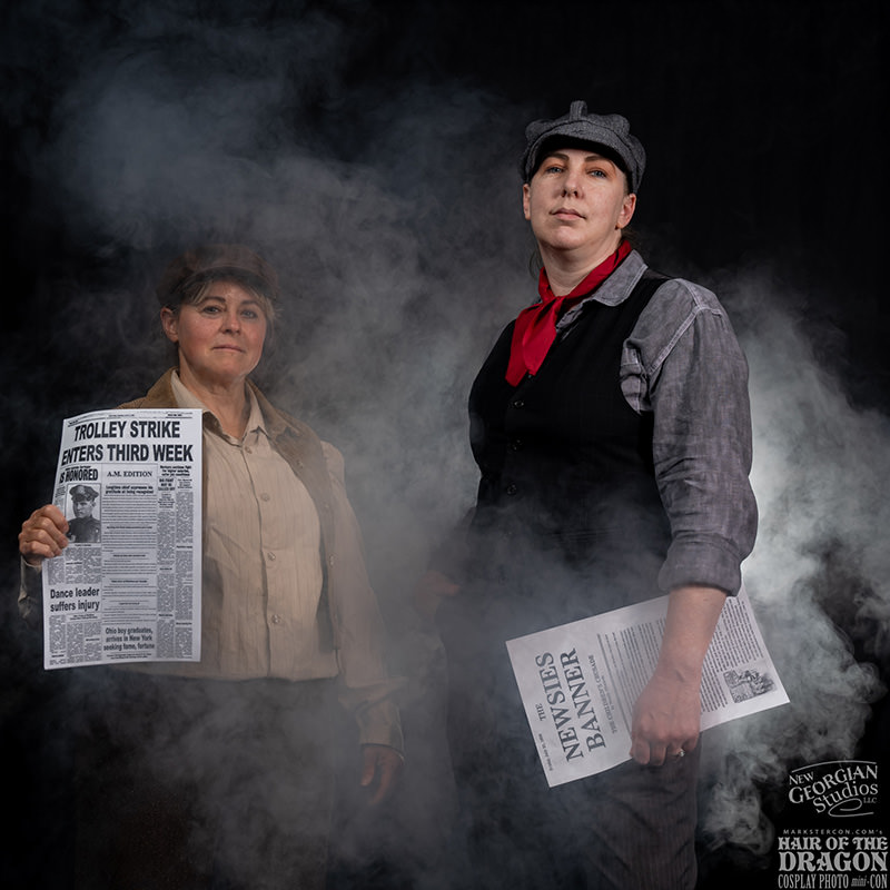 Two women in historical attire holding newspapers with headlines about a trolley strike, standing confidently amidst smoke with a dark background