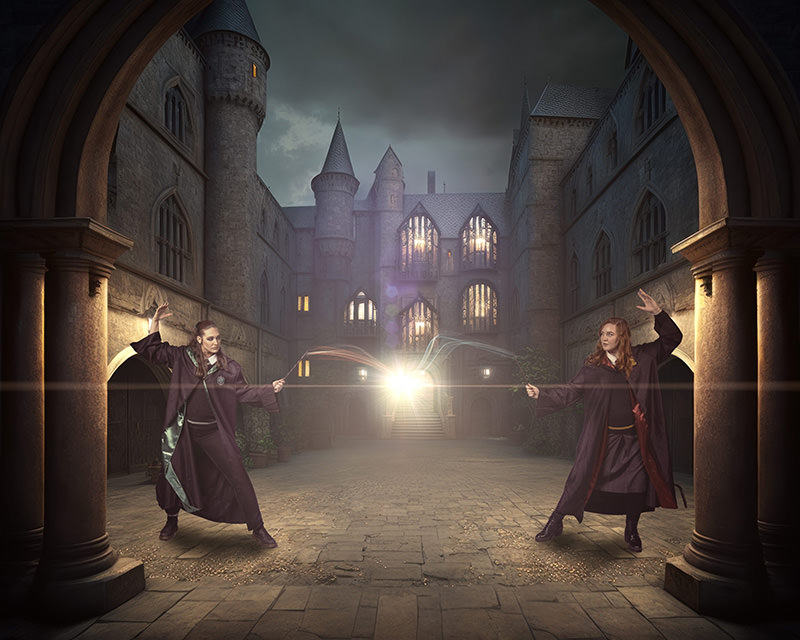 Two individuals in wizard robes casting spells at each other with glowing light between their wands, set in a medieval stone castle courtyard under a cloudy sky.